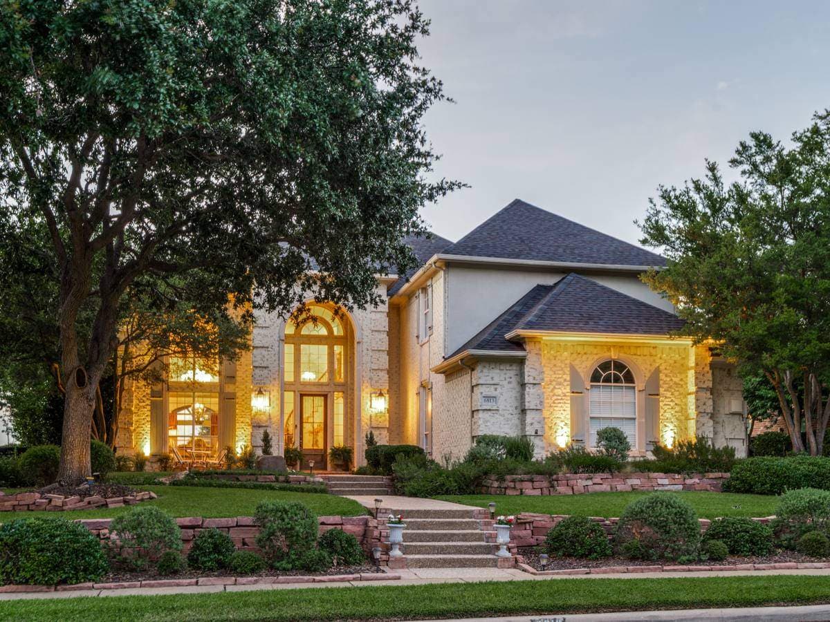Front exterior of a Sirka-listed DFW home glowing at dusk, with a landscaped stone-terraced lawn